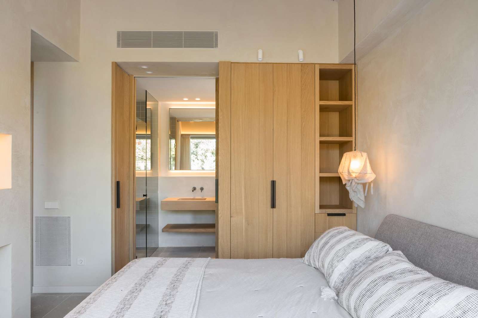 A minimalist bedroom with a hanging pendant light and wood cabinetry.