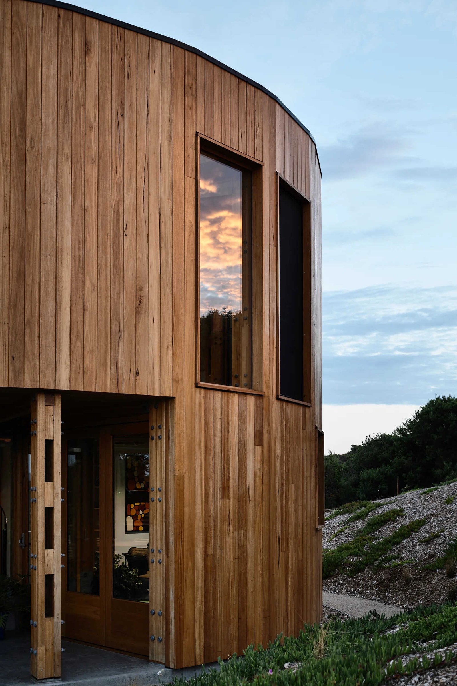 A round beach house with an integrated deck that opens directly to the surrounding sand dunes and bush.