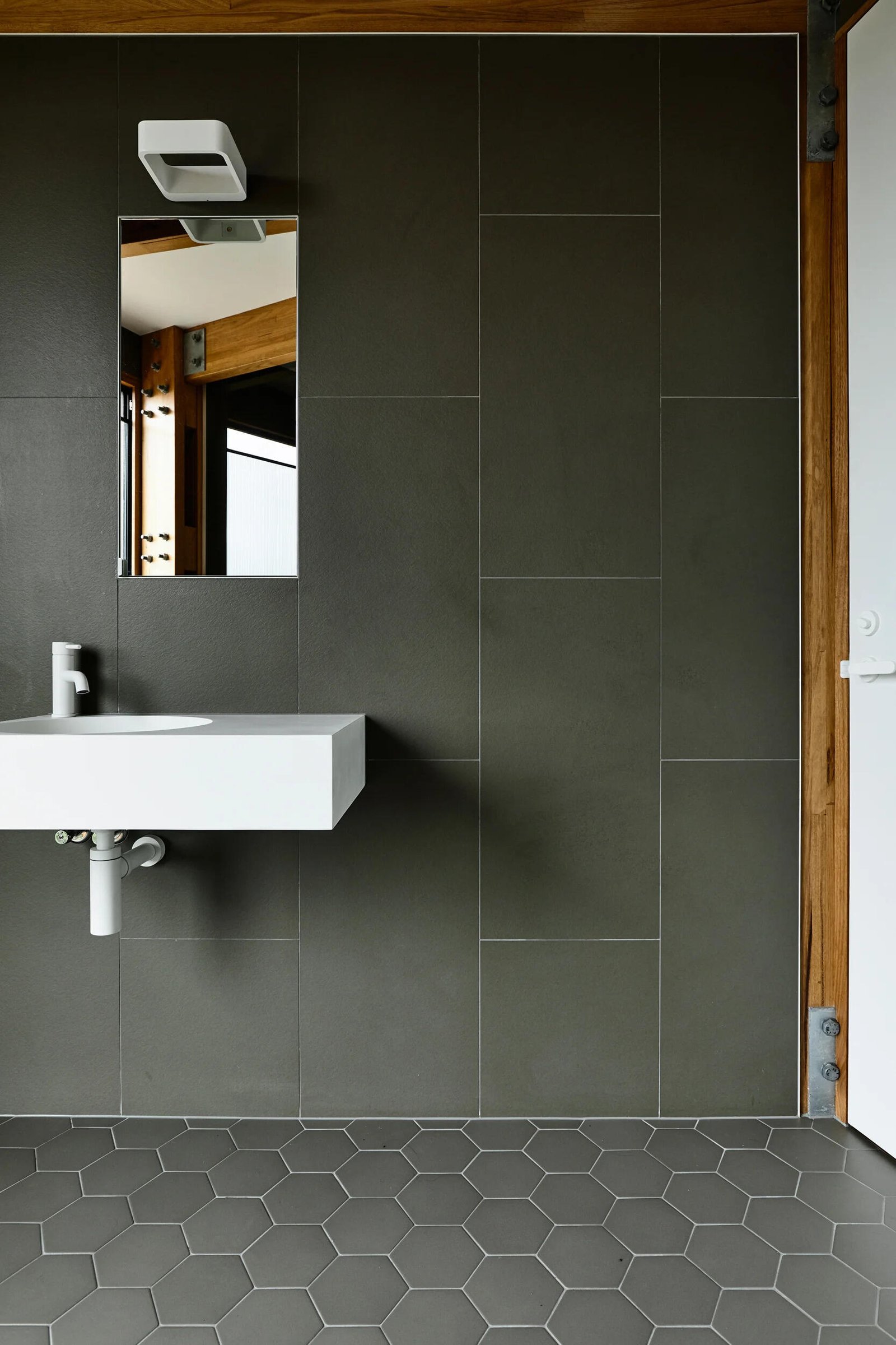 A minimalist bathroom with large format wall tiles and hexagonal floor tiles in a beach house setting.