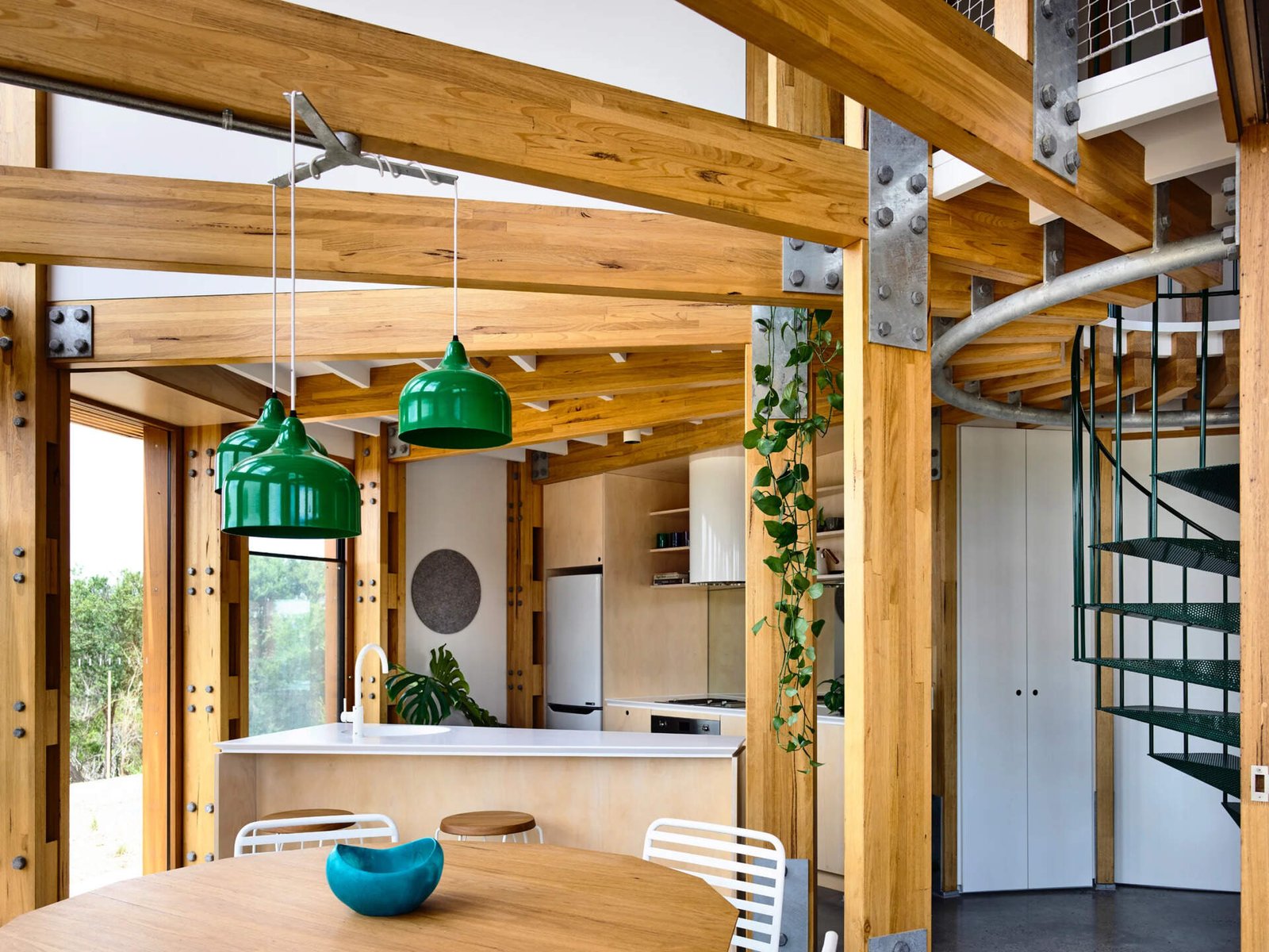 Open plan kitchen, dining and living areas inside a compact circular beach house designed for shared living.