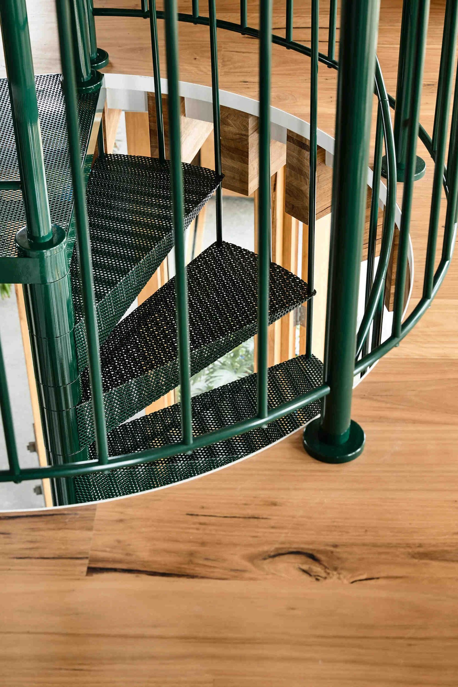 A dark green spiral staircase at the centre of a circular beach house interior.