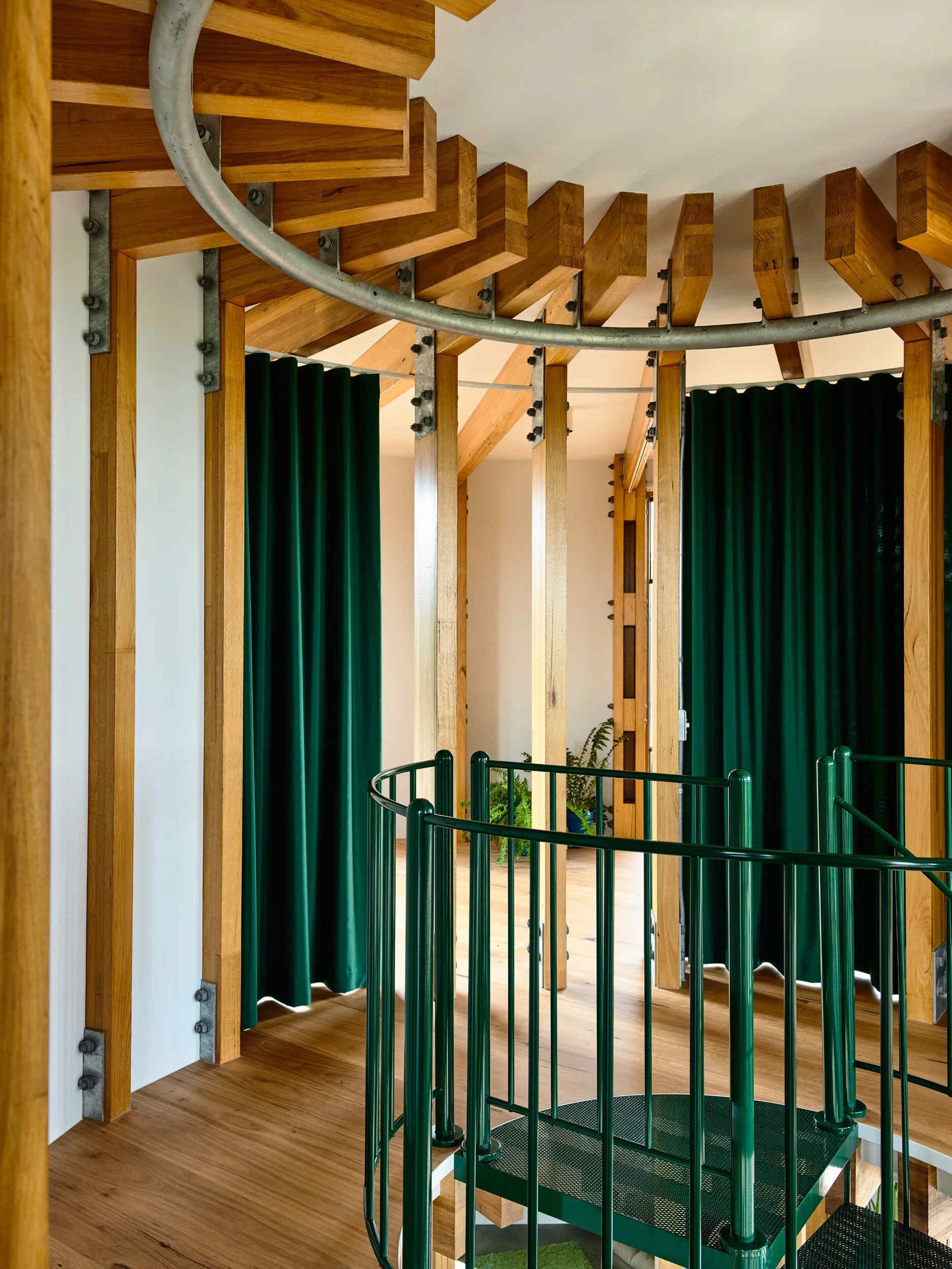 A dark green spiral staircase at the centre of a circular beach house interior.