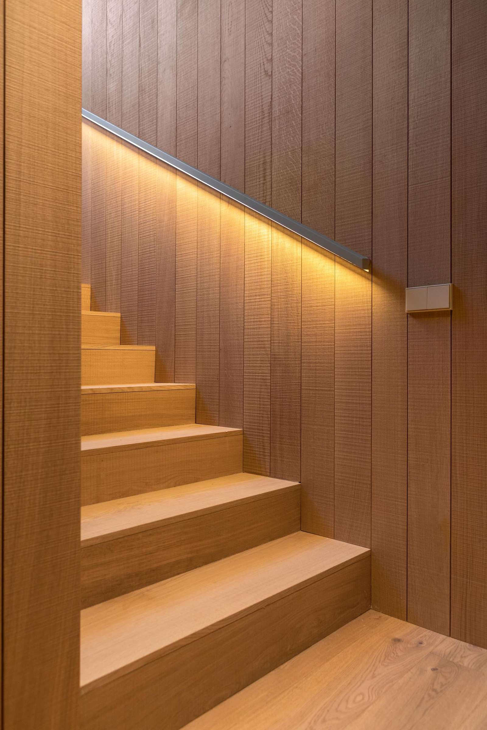 Modern wood stairs with a handrail that has hidden lighting.