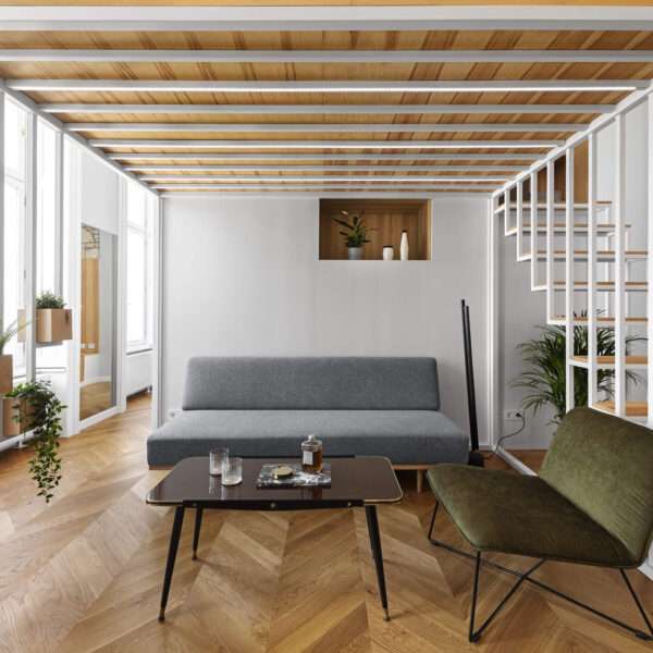 A calm living space with built in wood storage, indoor plants, and doors opening to a small balcony in the heart of Budapest.