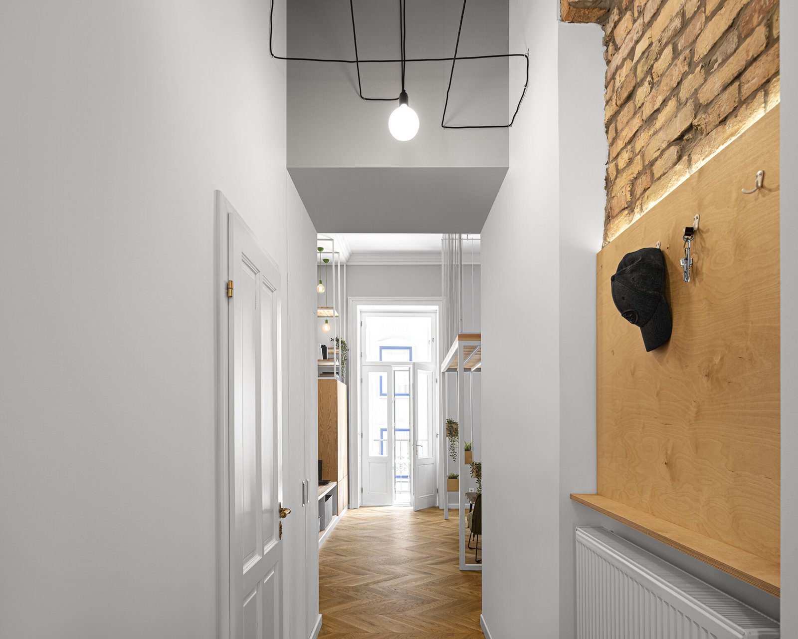 A narrow hallway transformed with exposed brick glimpses that connect the apartment’s historic structure to its modern interior design.