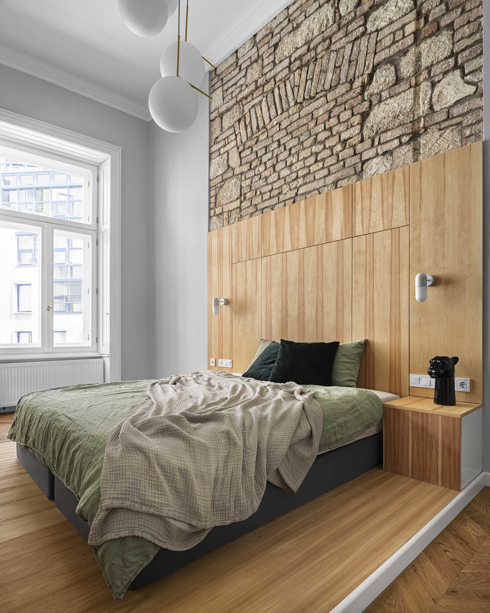 A high ceiling bedroom with exposed brick and stone, designed to shift easily from sleeping area to home office.