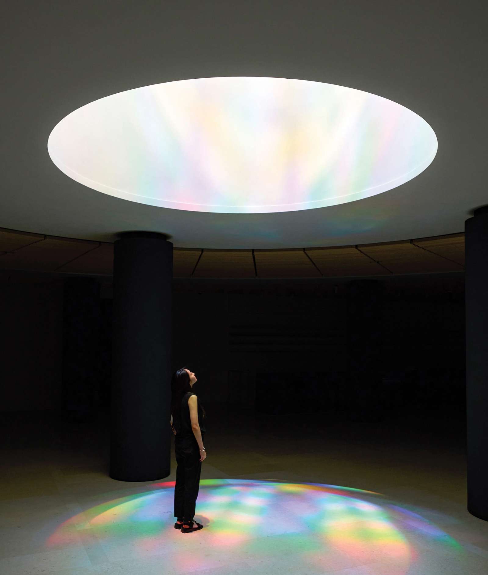 a person looks up at an opening with color and light streaming down