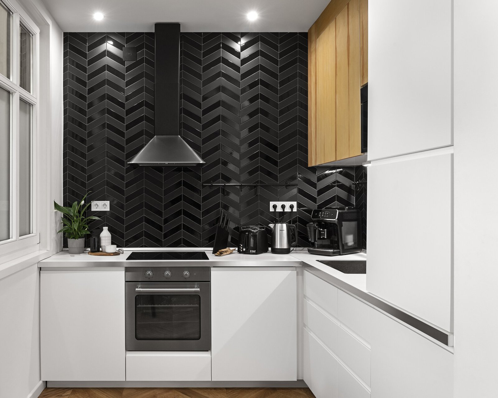 A bright open kitchen in a Budapest apartment featuring white cabinetry, black tile accents, and a minimalist dining setup designed for modern living.