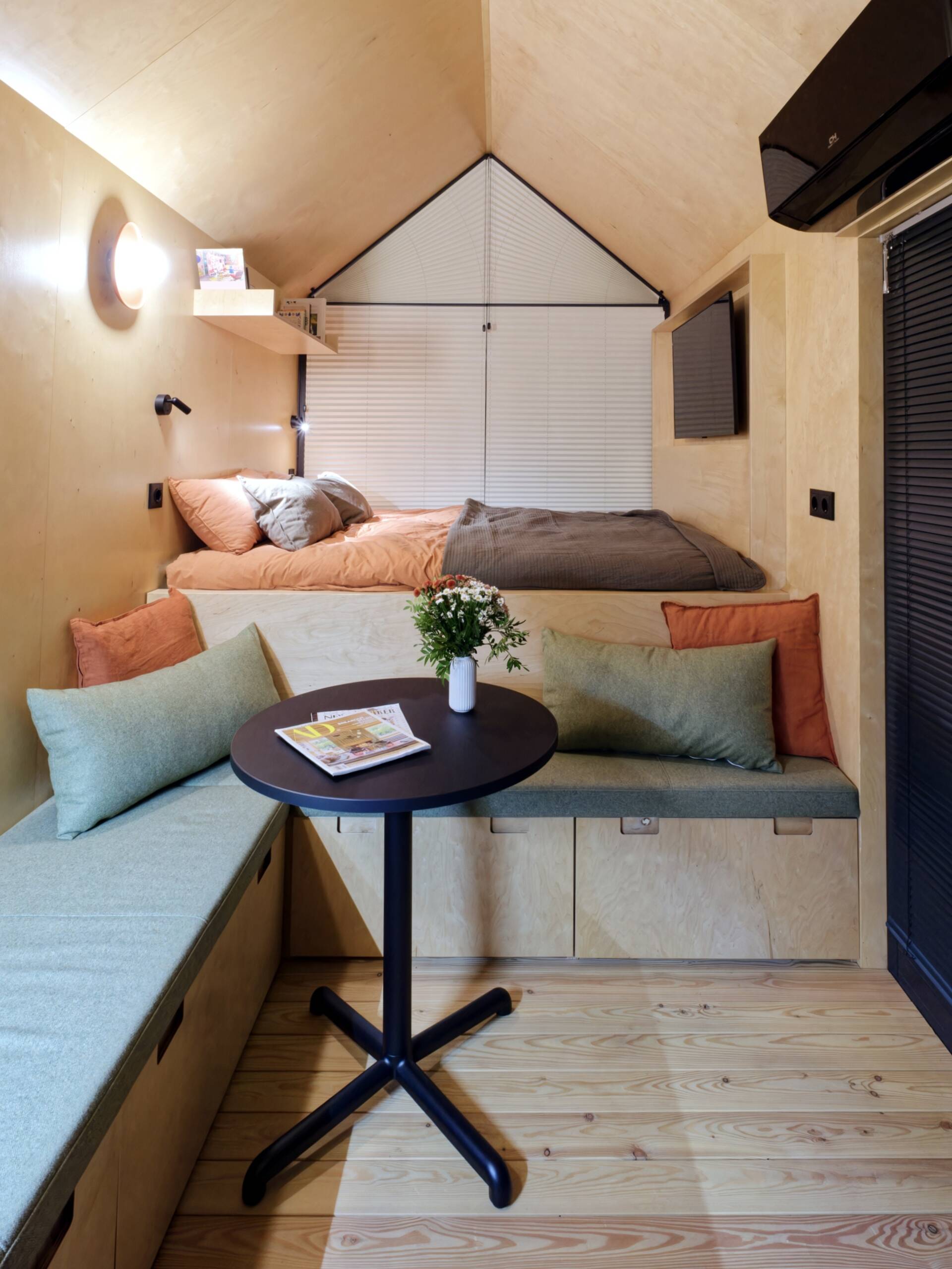 Light birch plywood, a visible gabled roof, and a striking trapezoidal window make this micro cabin interior feel surprisingly spacious. Included in the cabin is a sleeping area, lounge, kitchen, loft, and bathroom.