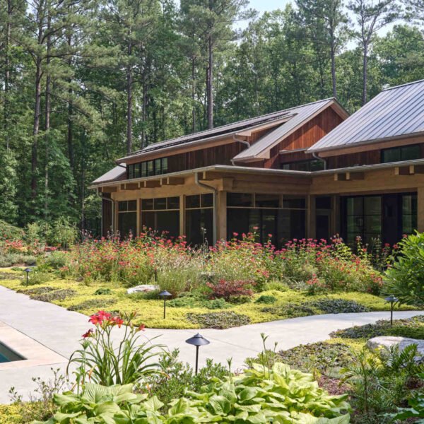 Double-height living, expansive windows, and a stone chimney define this warm, light-filled home in North Carolina, while an organized garden has room for a growing, relaxing, and enjoying the pool.
