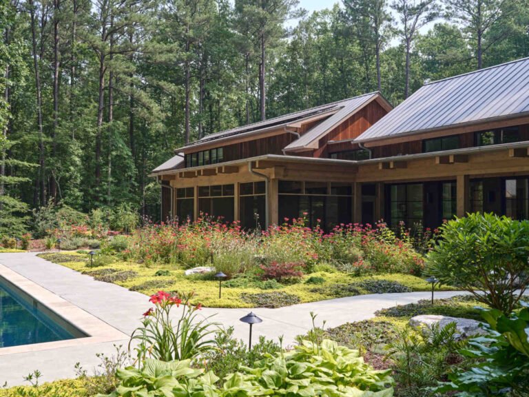 Double-height living, expansive windows, and a stone chimney define this warm, light-filled home in North Carolina, while an organized garden has room for a growing, relaxing, and enjoying the pool.