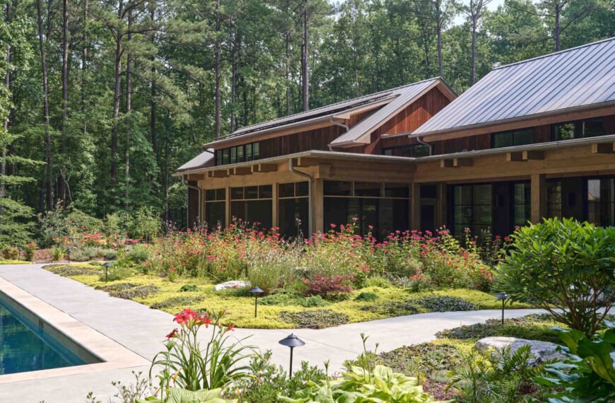 Double-height living, expansive windows, and a stone chimney define this warm, light-filled home in North Carolina, while an organized garden has room for a growing, relaxing, and enjoying the pool.