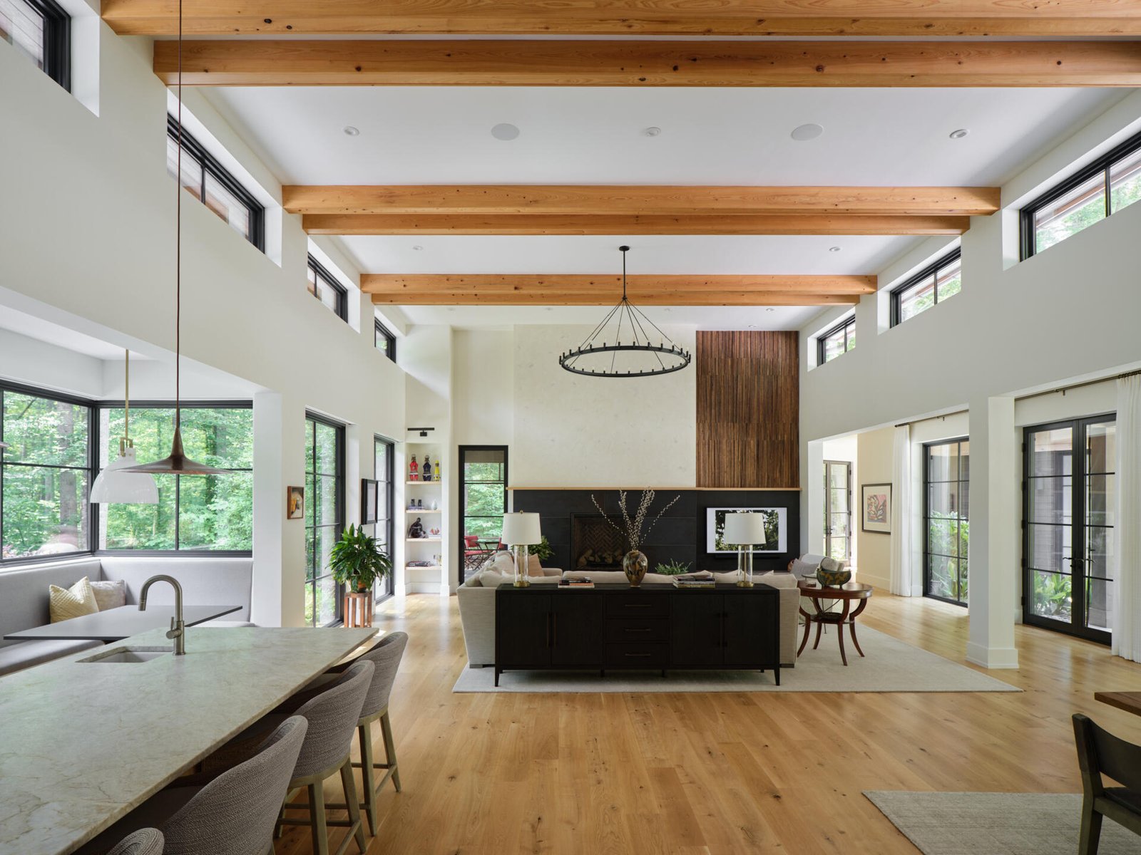 A double-height living room with a striking fireplace and large windows that frame the forest beyond.