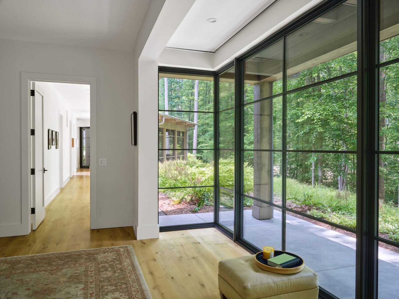 A window-lined hallway leads to the primary bedroom, pairing forest views with a gallery-style wall of art.