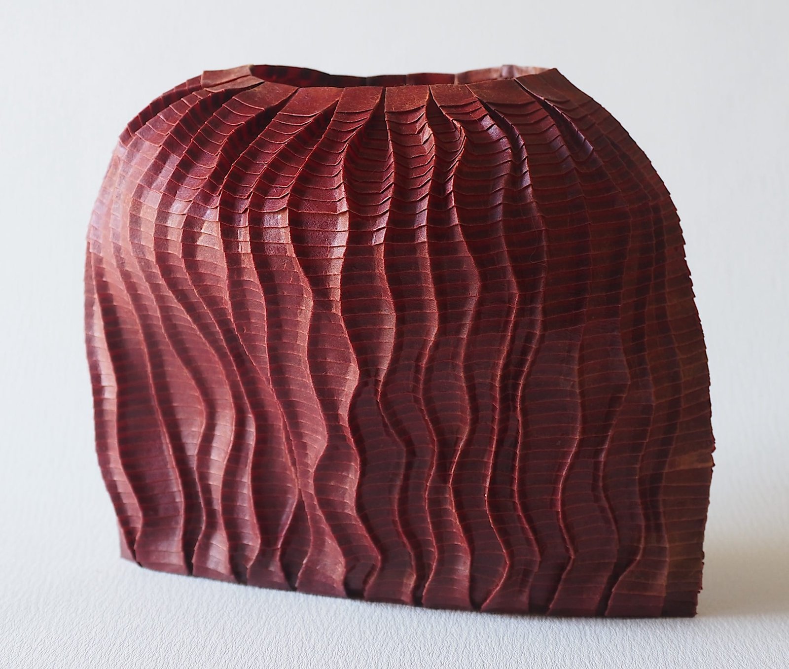 An origami paper vase made with dark red paper, with a wavy texture