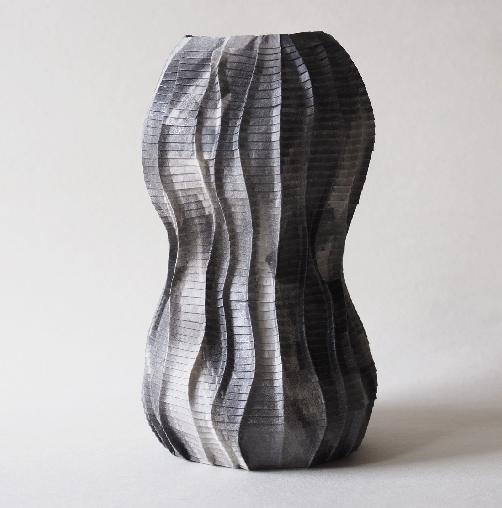An origami paper vase in gray paper with a wavy, ripple effect