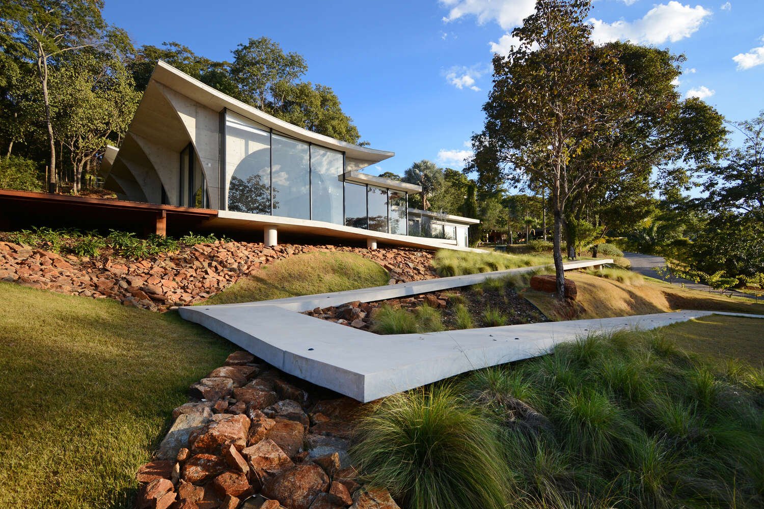 A winding concrete ramp leads up to Casa Joy in Brazil, revealing a sculptural modern home defined by six dramatic concrete arches and a concave roof overlooking the valley.