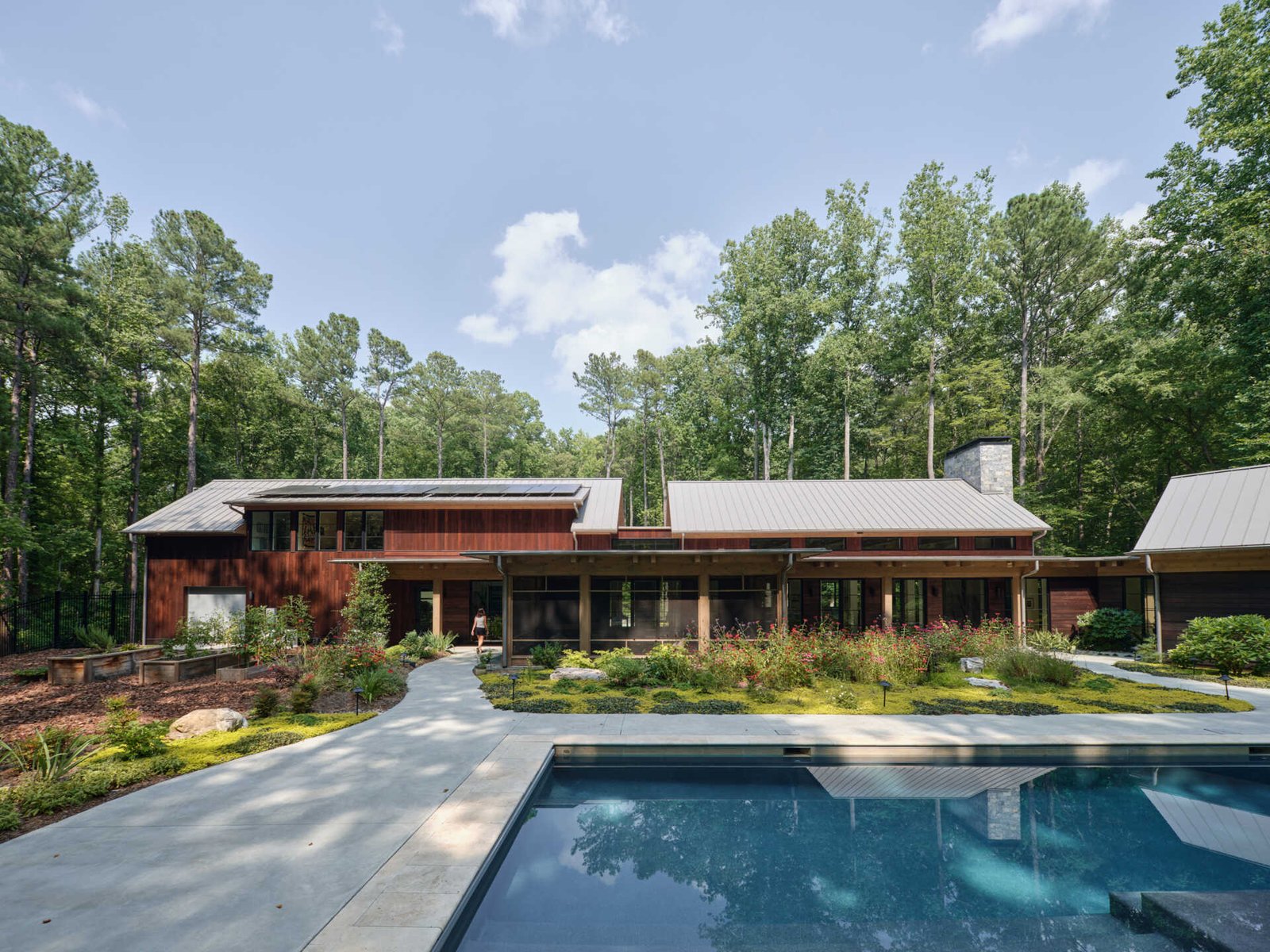 Double-height living, expansive windows, and a stone chimney define this warm, light-filled home in North Carolina, while an organized garden has room for a growing, relaxing, and enjoying the pool.