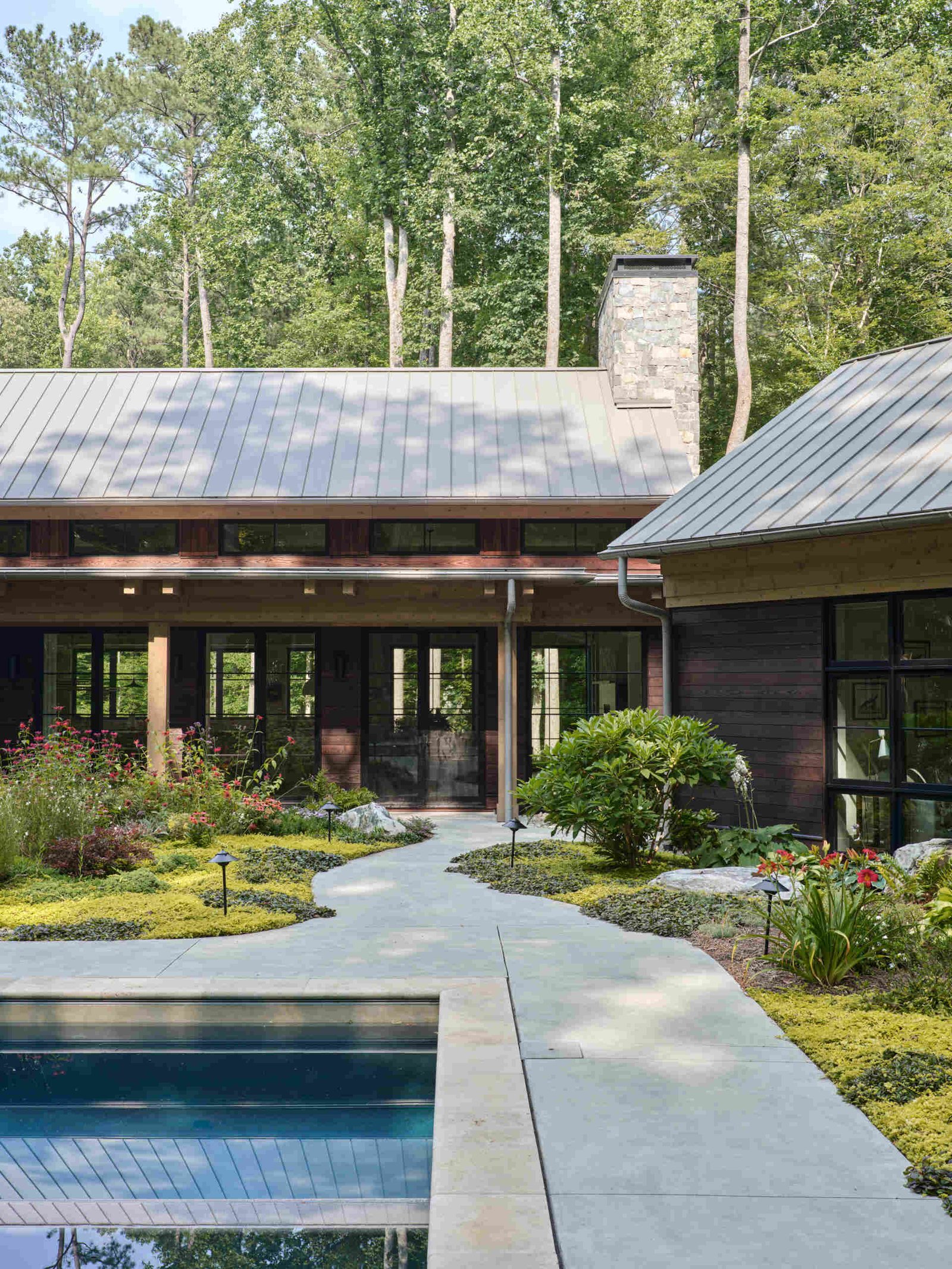 Double-height living, expansive windows, and a stone chimney define this warm, light-filled home in North Carolina, while an organized garden has room for a growing, relaxing, and enjoying the pool.