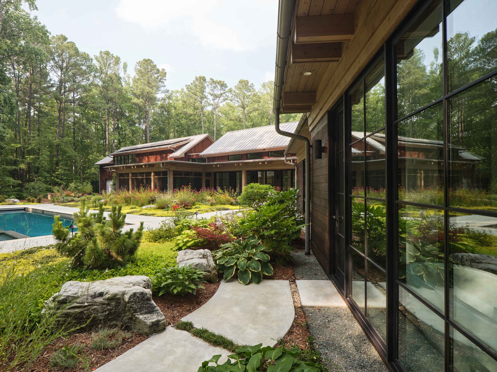 Double-height living, expansive windows, and a stone chimney define this warm, light-filled home in North Carolina, while an organized garden has room for a growing, relaxing, and enjoying the pool.