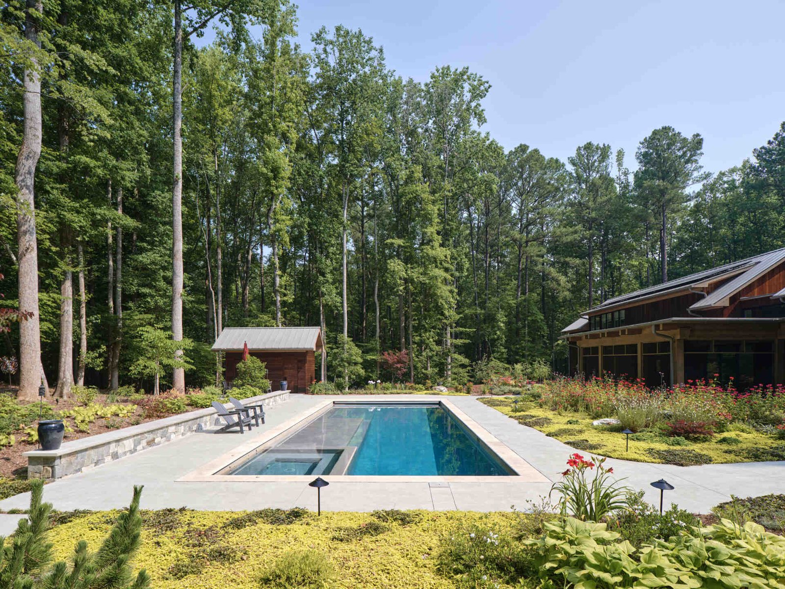 Double-height living, expansive windows, and a stone chimney define this warm, light-filled home in North Carolina, while an organized garden has room for a growing, relaxing, and enjoying the pool.