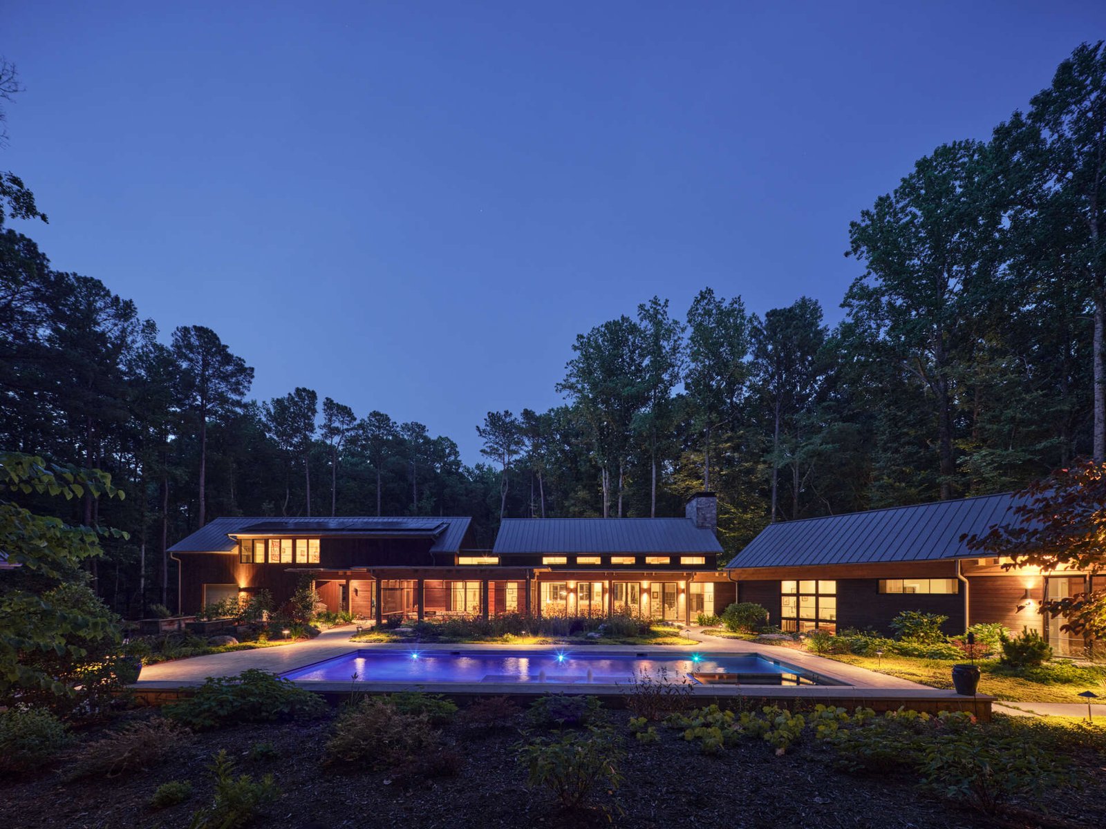 Double-height living, expansive windows, and a stone chimney define this warm, light-filled home in North Carolina, while an organized garden has room for a growing, relaxing, and enjoying the pool.