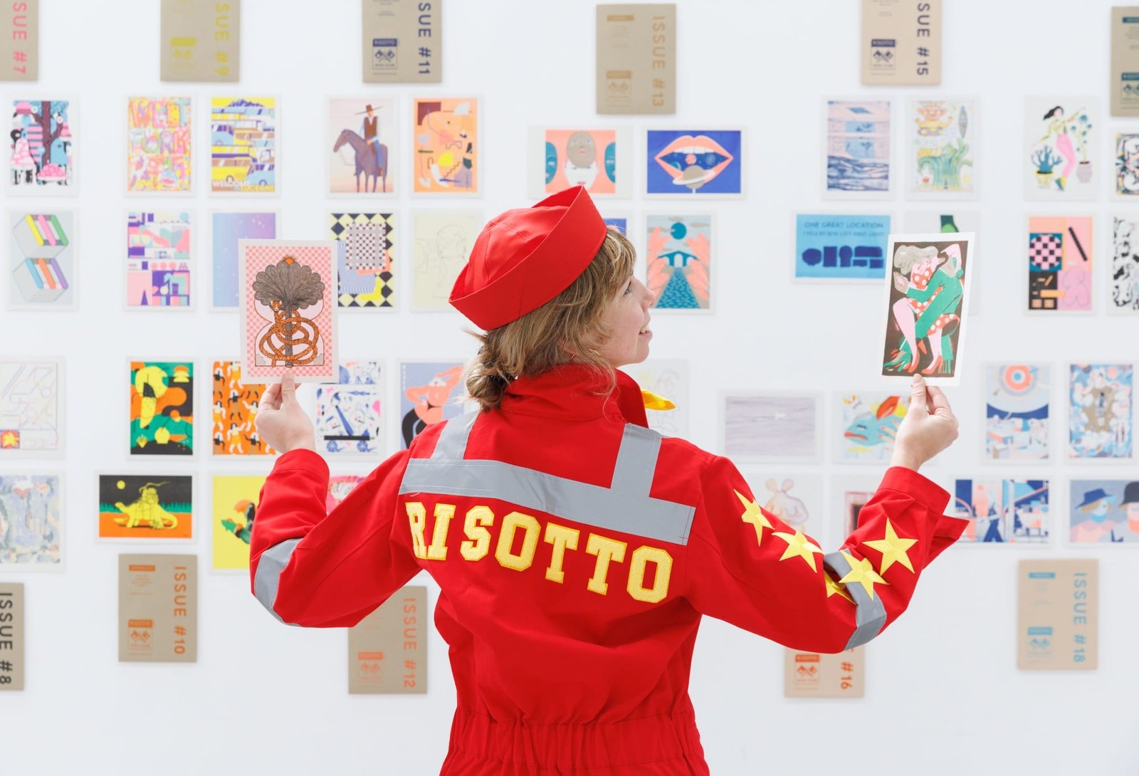 a person in a red suit stands in front of a wall of riso prints