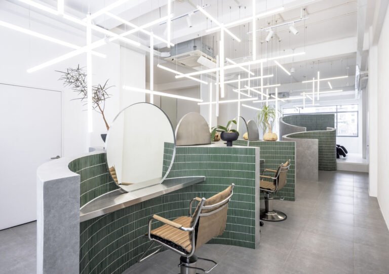 A hair salon in Ho Chi Minh City designed by Inrestudio, shaped by a continuous sculptural wall that guides movement through waiting areas, styling stations, and shampoo spaces. The interior shifts between green tile and raw grey surfaces, with light and form changing as you move through each level of the maisonette.