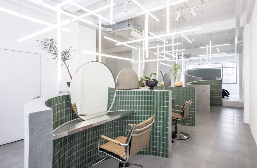 A hair salon in Ho Chi Minh City designed by Inrestudio, shaped by a continuous sculptural wall that guides movement through waiting areas, styling stations, and shampoo spaces. The interior shifts between green tile and raw grey surfaces, with light and form changing as you move through each level of the maisonette.