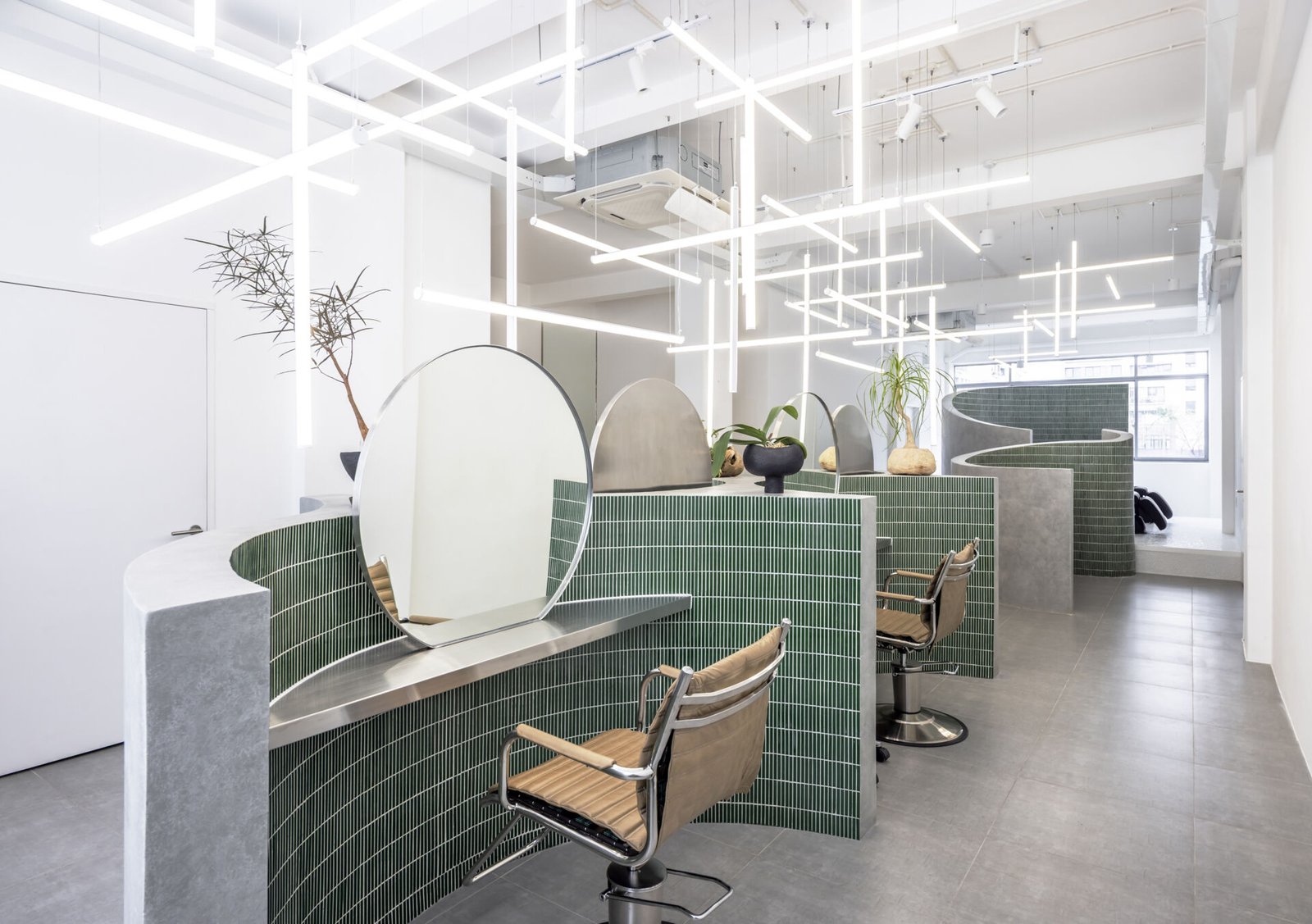 A hair salon in Ho Chi Minh City designed by Inrestudio, shaped by a continuous sculptural wall that guides movement through waiting areas, styling stations, and shampoo spaces. The interior shifts between green tile and raw grey surfaces, with light and form changing as you move through each level of the maisonette.