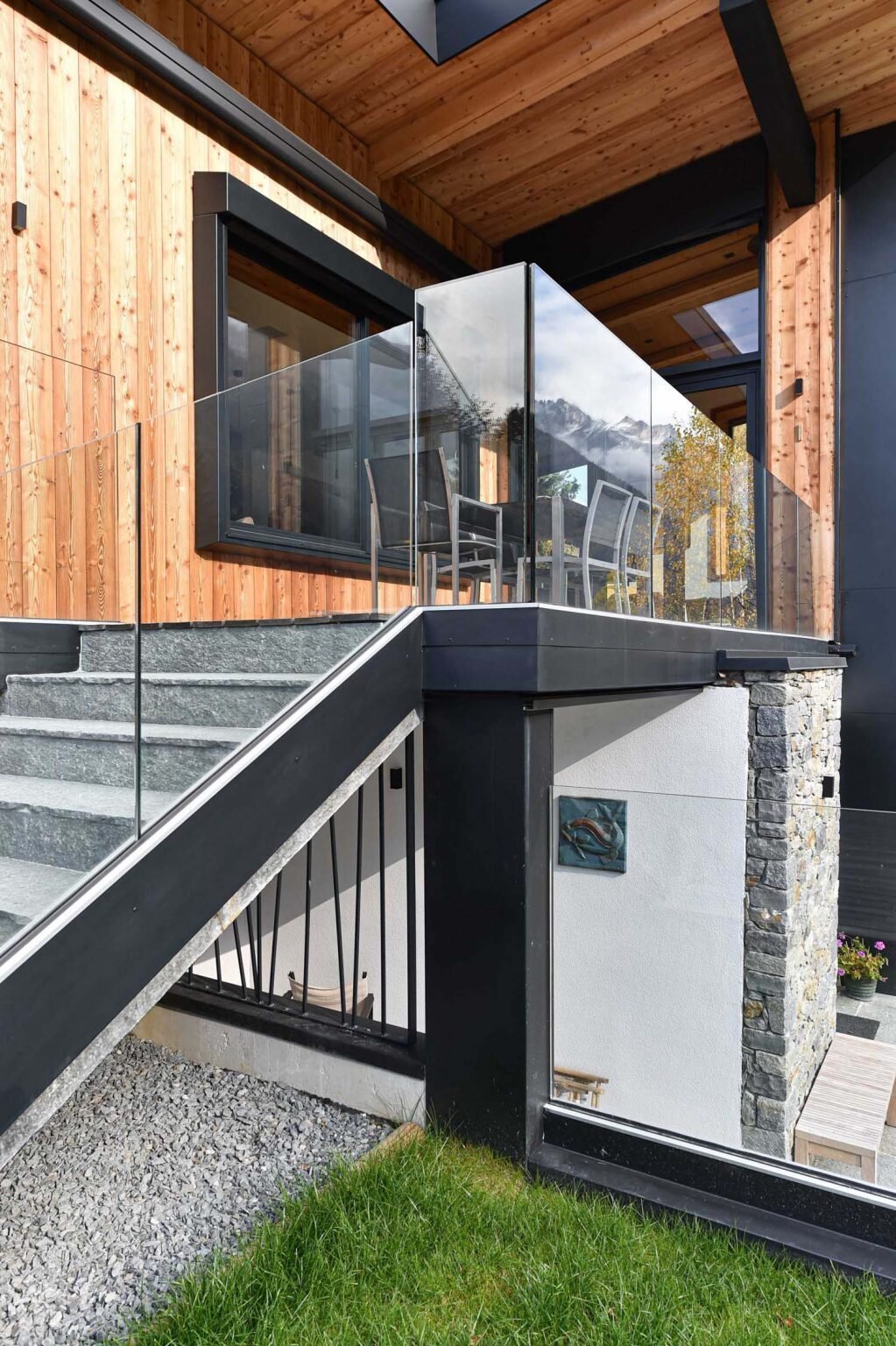Glass railings, wood siding, and mountain views define the outdoor spaces of this modern alpine home in Chamonix, France.