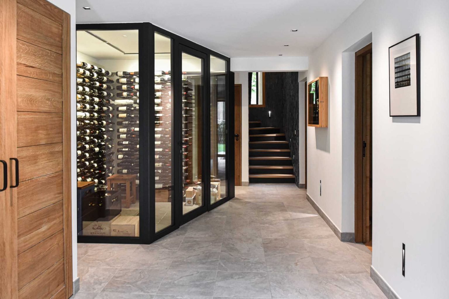 A glass-enclosed wine cellar beneath the staircase adds a dramatic and luxurious feature to this renovated Chamonix residence.