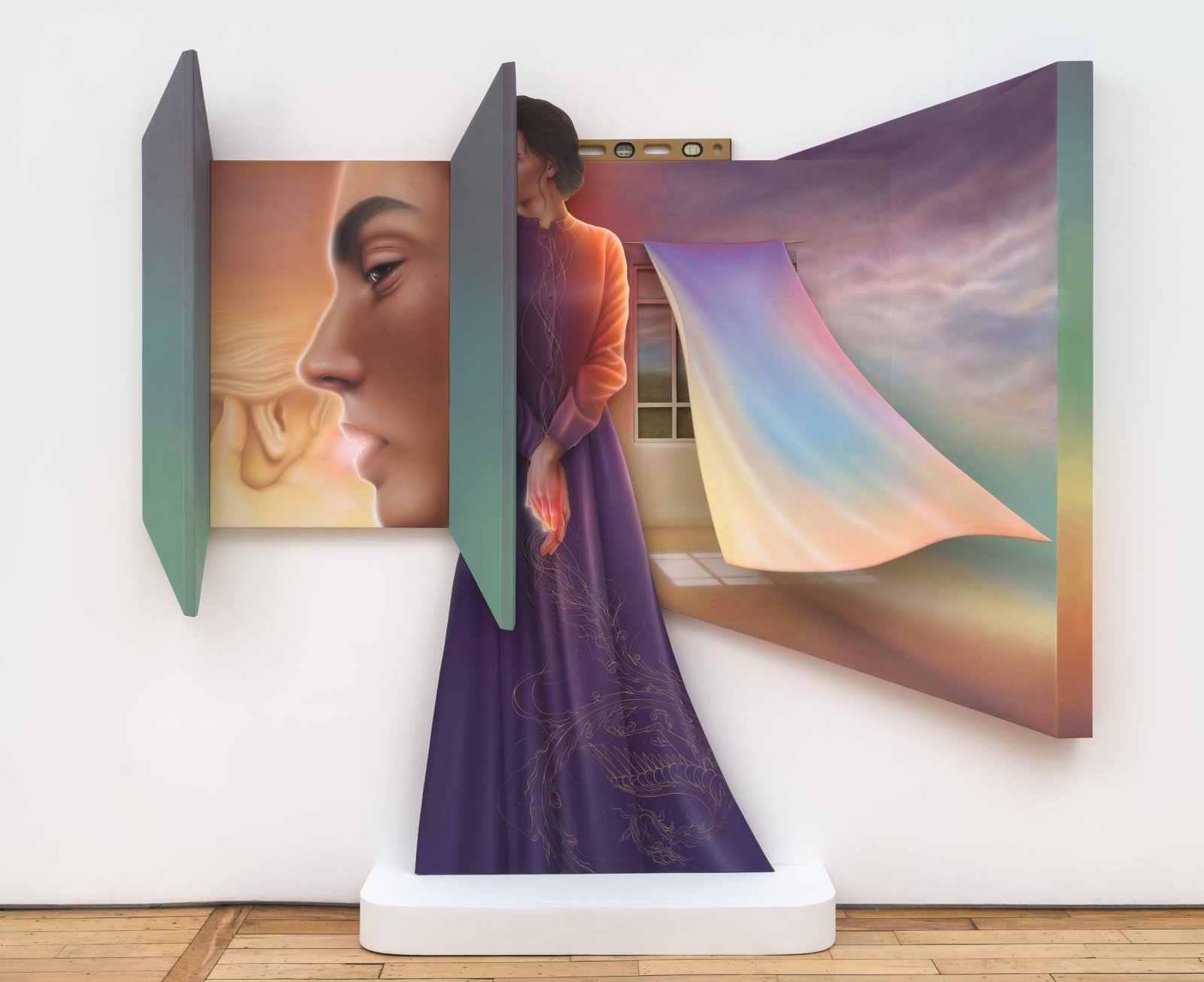 a colorful sculpture of a standing woman in the center with a drape blowing on the right and a closeup of a face on the left