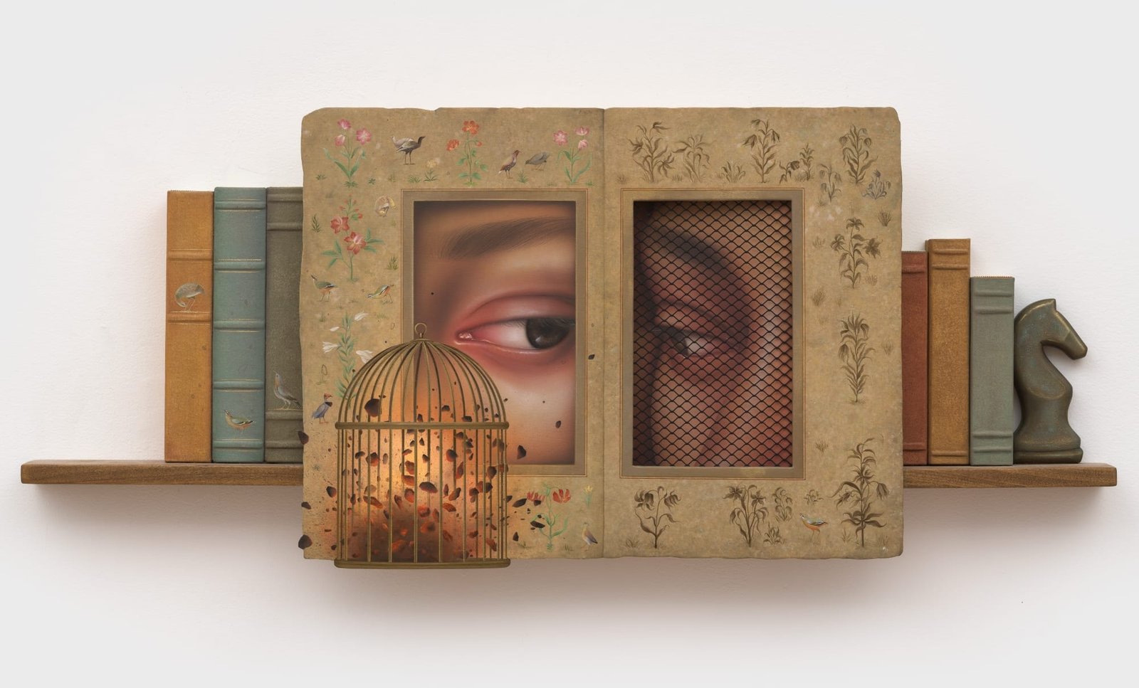 a shelf like sculpture with books, a horse shaped bookend, and a frame with two eyes peering at each other. a bird cage is in front