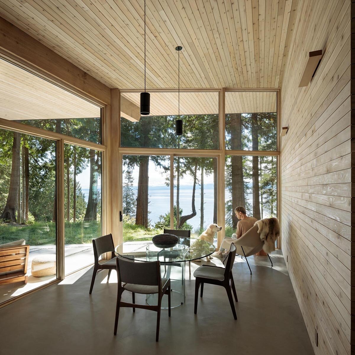 A dining space with a wood feature wall and concrete floors flows into a kitchen with thick countertops and dark cabinetry.