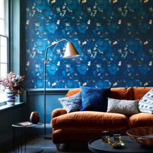 غرفة معيشة مع ورق حائط مزخرف باللون الأزرق وأريكة برتقالية ومصباح نحاسي