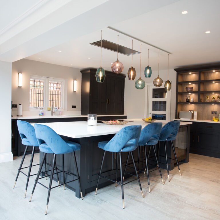 White kitchen with island, blue bar chairs and coloured pendant lighting