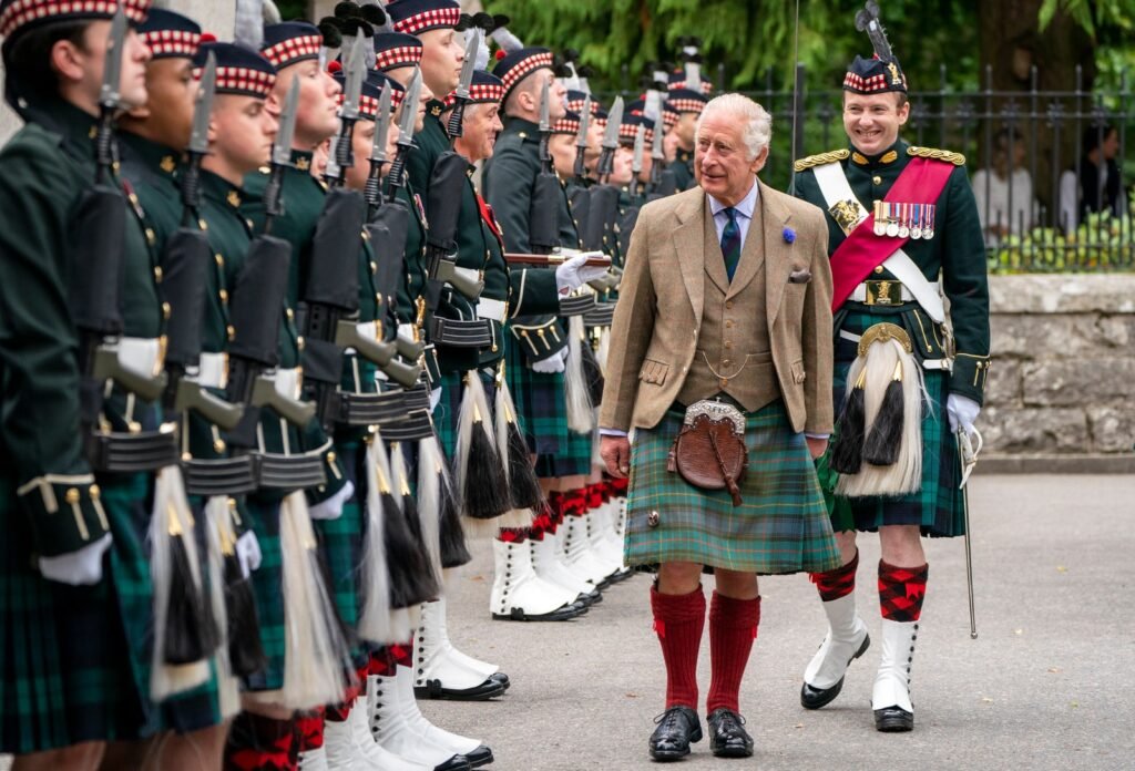 King Charles III at Balmoral castle grounds wearing a kilt walking alongside a line of royal staff