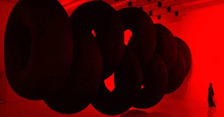 nine colossal tubes undulate and dwarf visitors amid a red glow in SpY’s beijing installation