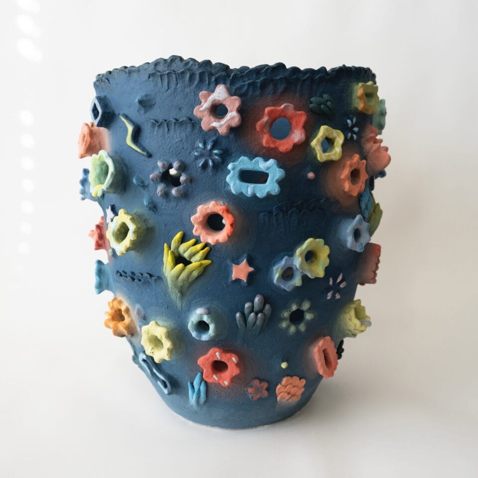 a ceramic vase with a number of colorful flower blossoms on a blue background