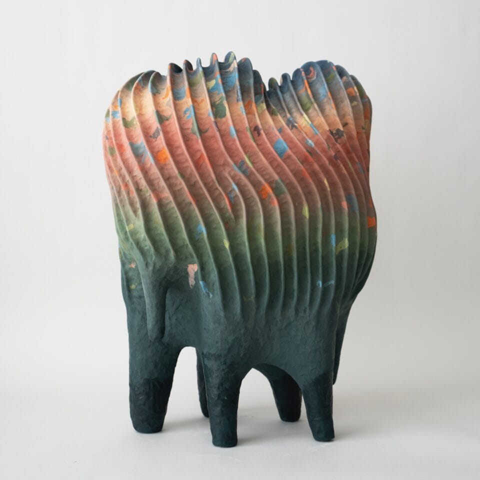 an abstract, colorful ceramic sculpture with a linear texture and a color gradient from green to orange to yellow