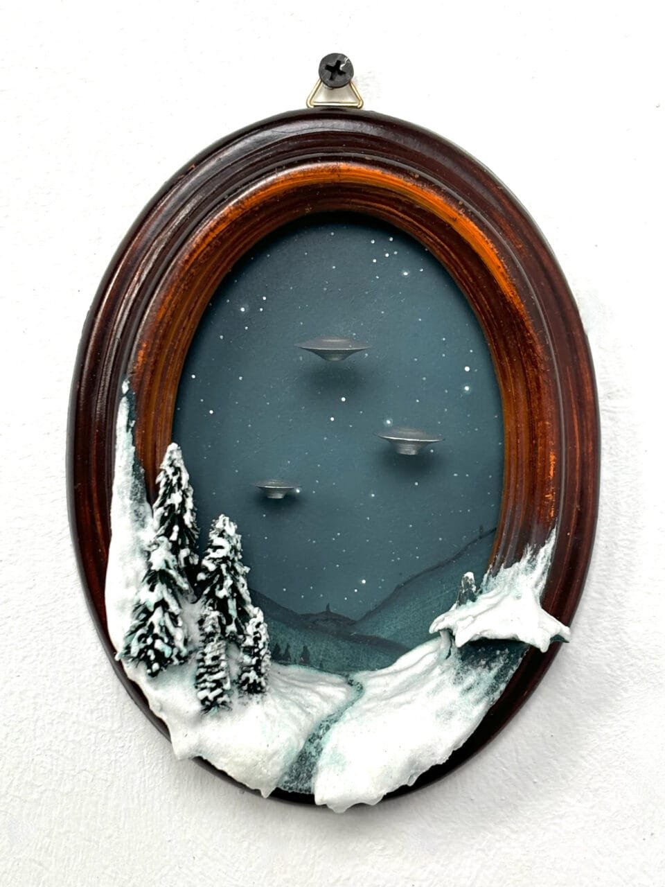 within a miniature ovoid frame, a detailed diorama depicts a landscape with hovering UFOs