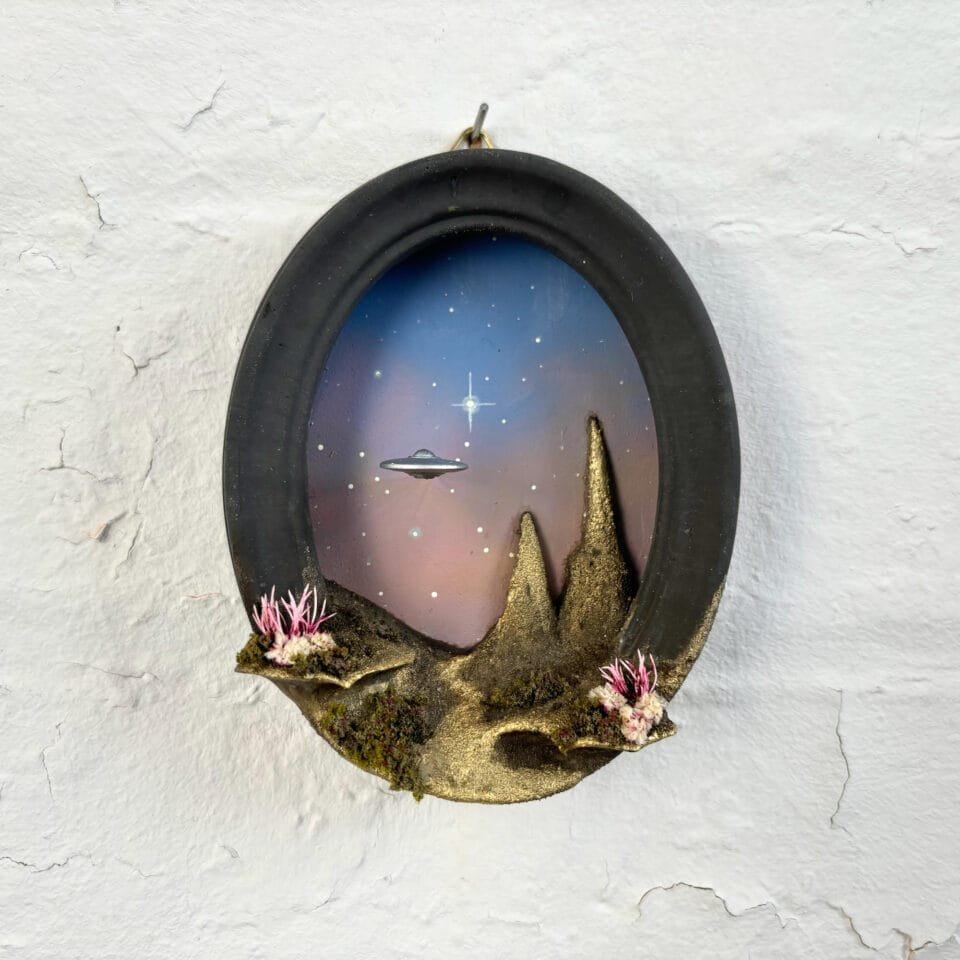 within a miniature ovoid frame, a detailed diorama depicts a landscape with a hovering UFO