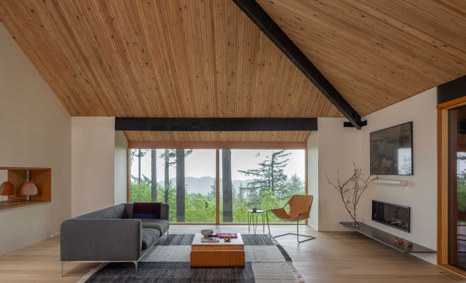 In this living room, the exposed beams have been refurbished and finished in black, while a nail-laminated ceiling is shown throughout. There's also a custom built-in bar with sliding mirror doors, and on the opposite wall, a fireplace with floating hearth.