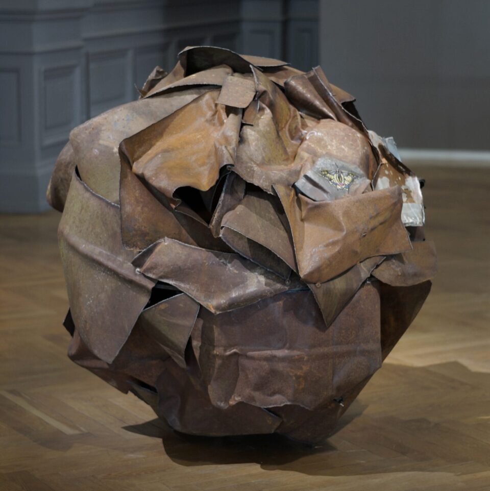 a large rusted ball of metal with a cross-stitched butterfly in one area
