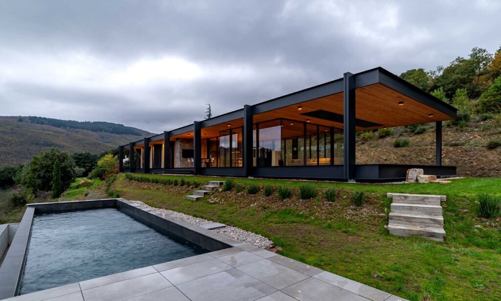 A modern house with a horizontal layout, walls of glass, and an exposed steel structure.