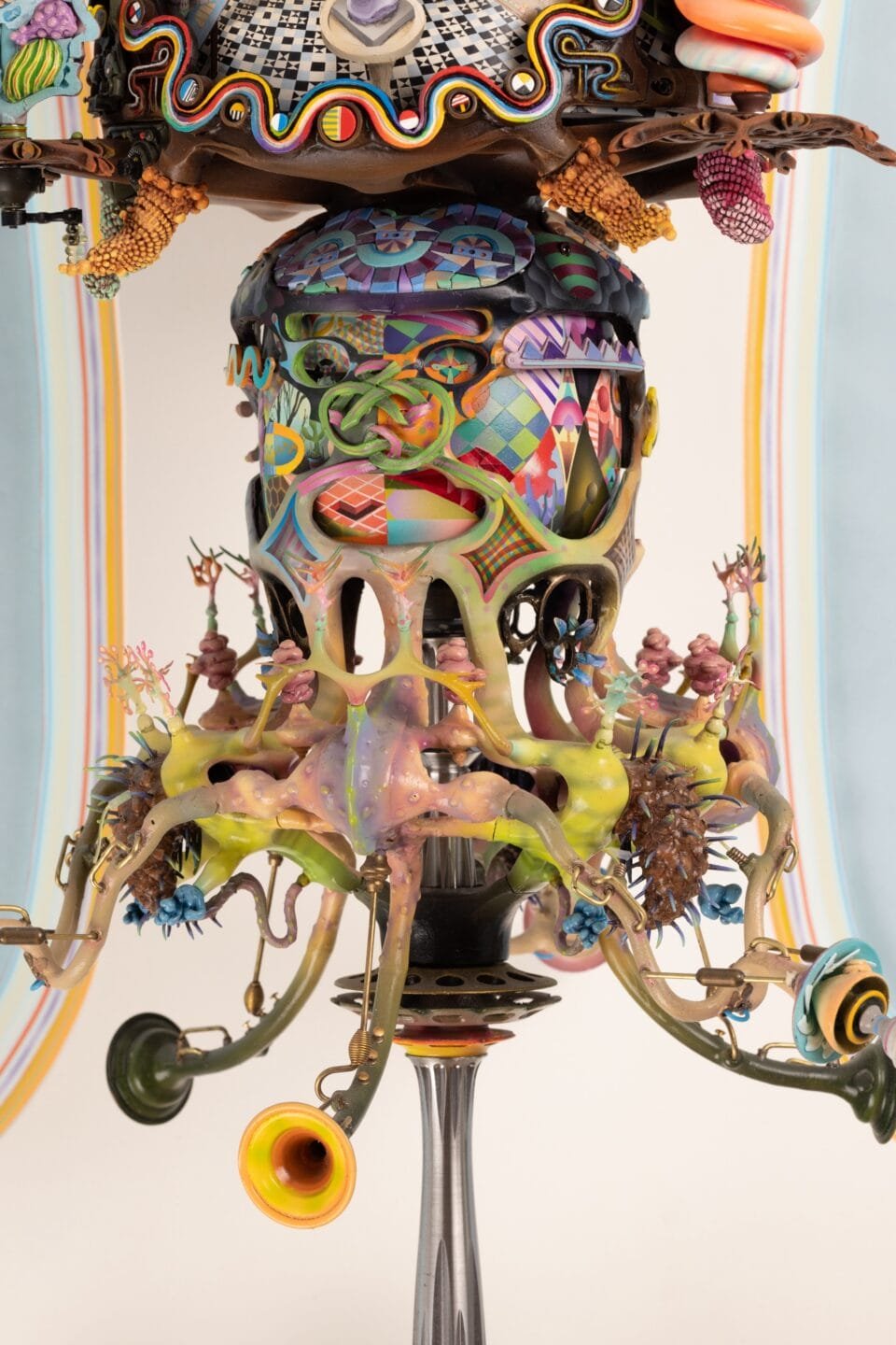 a detail of the lower part of an elaborately detailed sculpture with numerous sculpted, found, and painted elements installed on an ornately shaped white panel, with some of the elements able to be moved and rotated to show different scenes