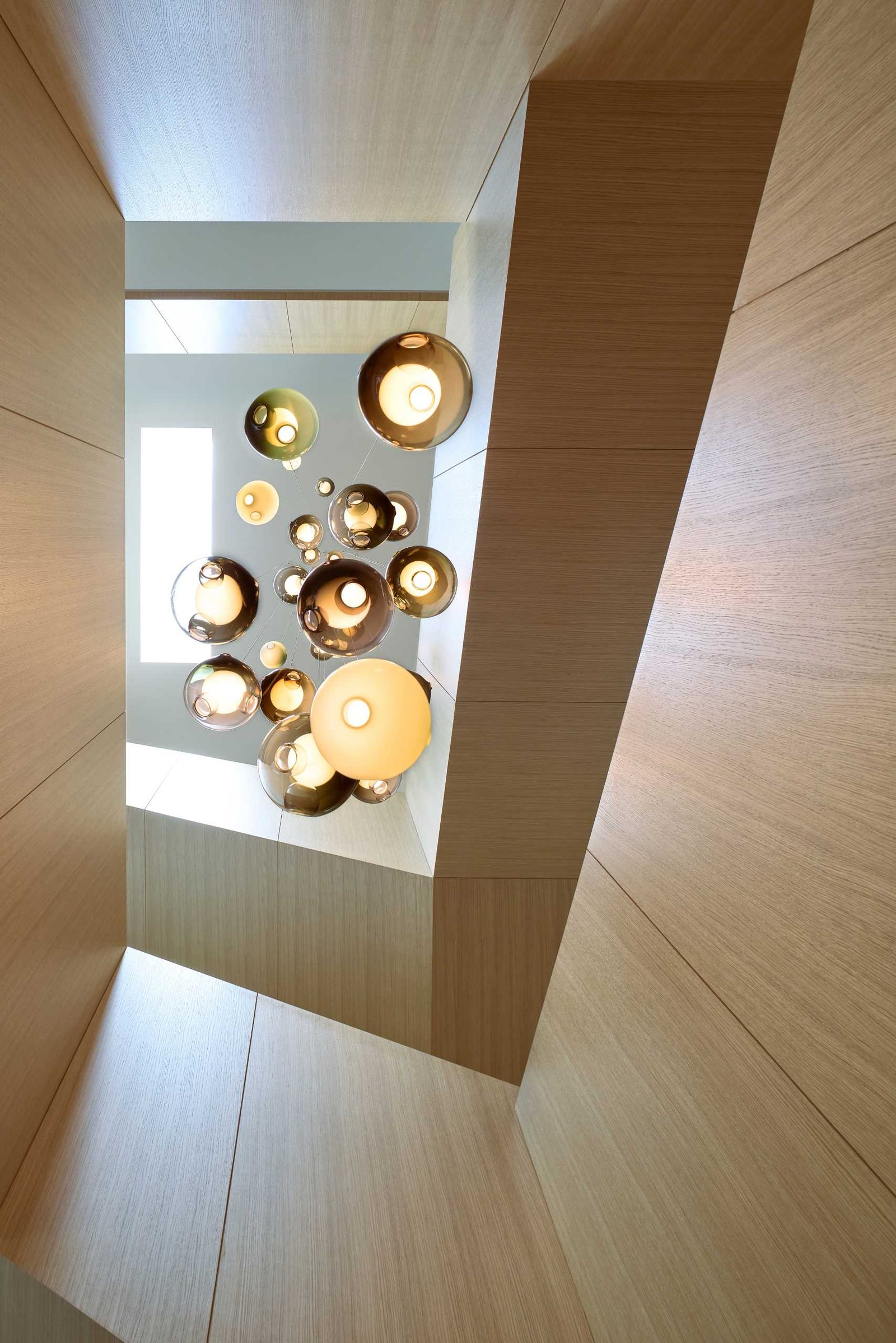 A standout architectural feature in this modern home is the grand oak staircase, which spirals around a suspended three-story glass chandelier.