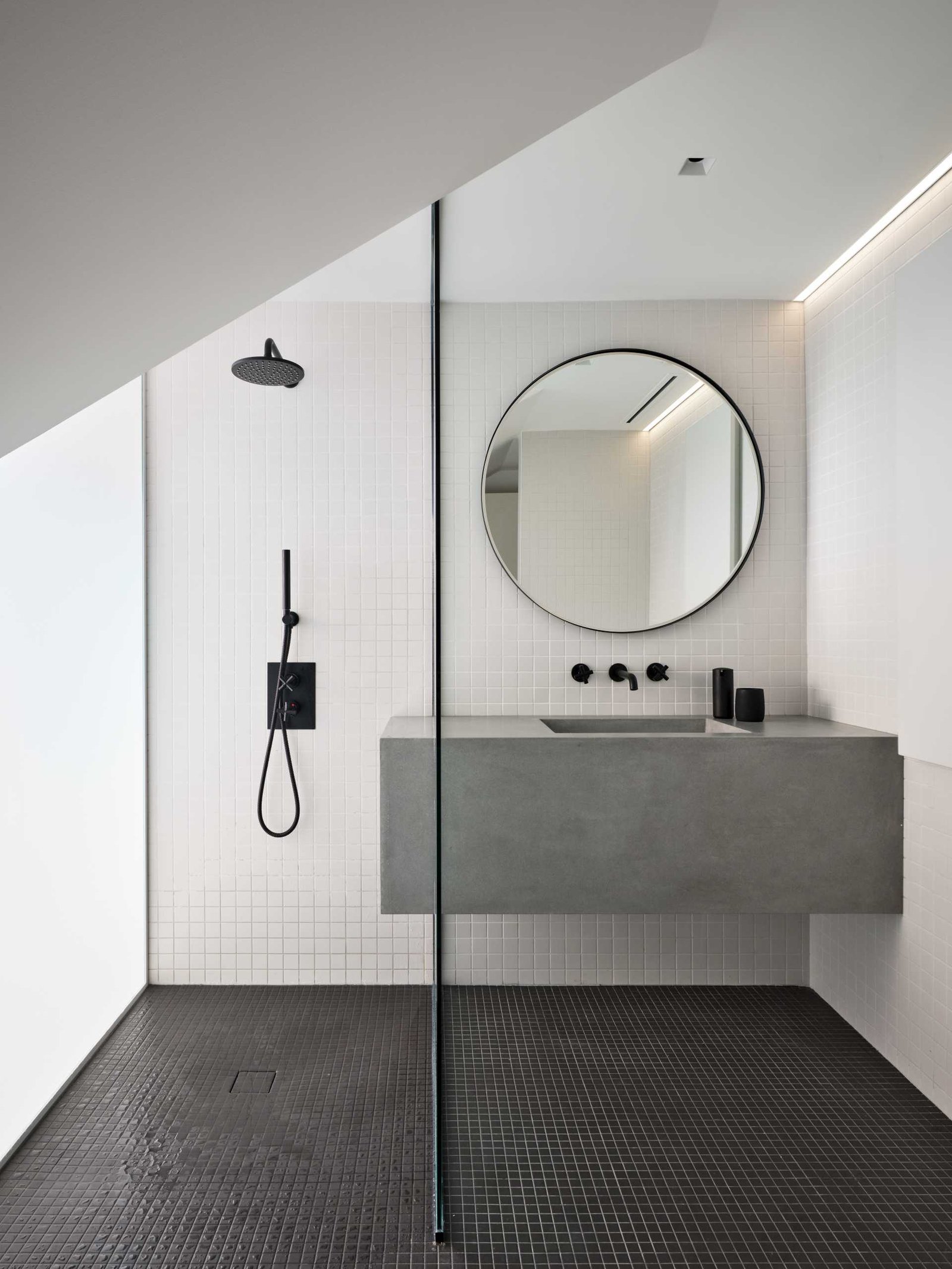 This bathroom is minimalist in its design, with square white tiles covering the walls, and black tiles on the floor.