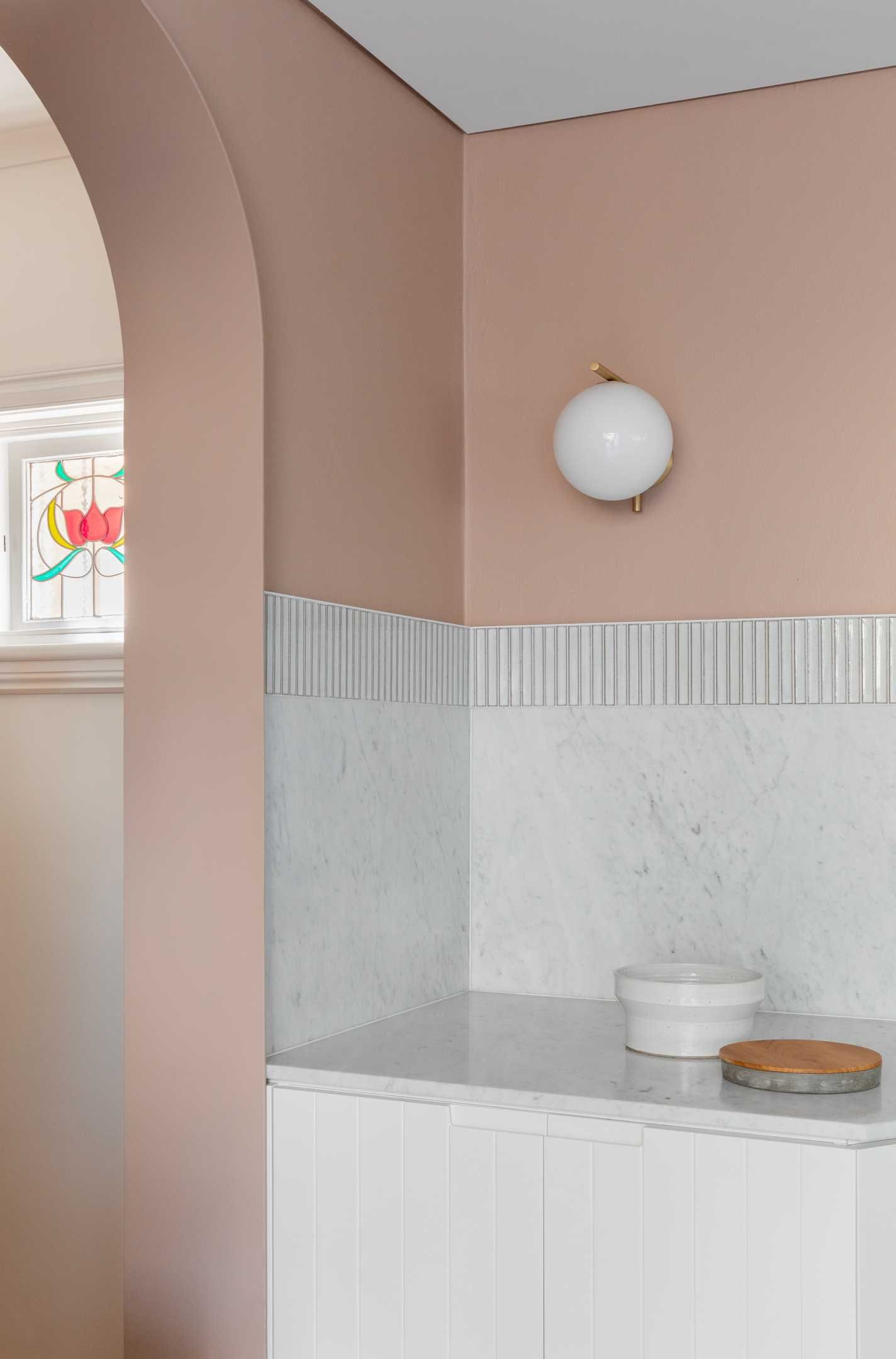 In this modern dining area, earthy peach painted above the tile datum helps to centre and hold the space, while a circular Jardan marble dining table is central to the space, and a curved timber panelled joinery lines the wall.